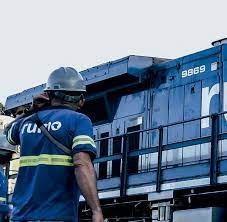 Homem de costas usando o uniforme da Rumo. Ao fundo um vagão da Rumo.